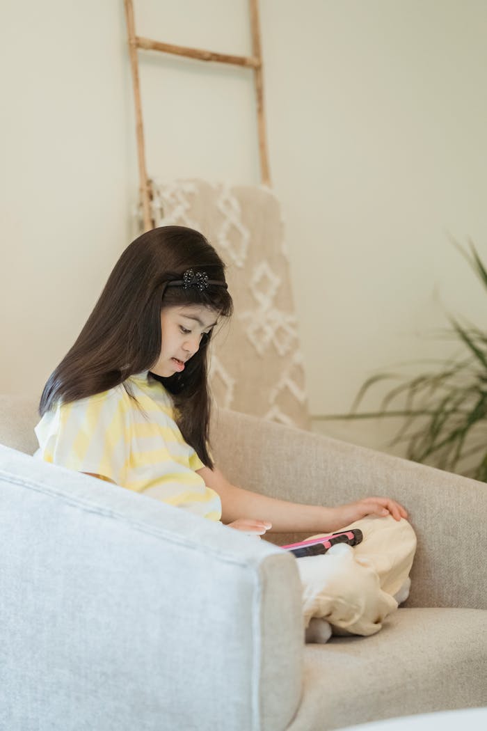 Child sitting on a sofa with a tablet, wearing a yellow dress, indoors.